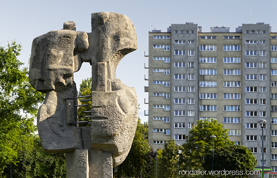 Itinerari per Nowa Huta. Escultura abstracte en un parc amb un bloc gris de fons.