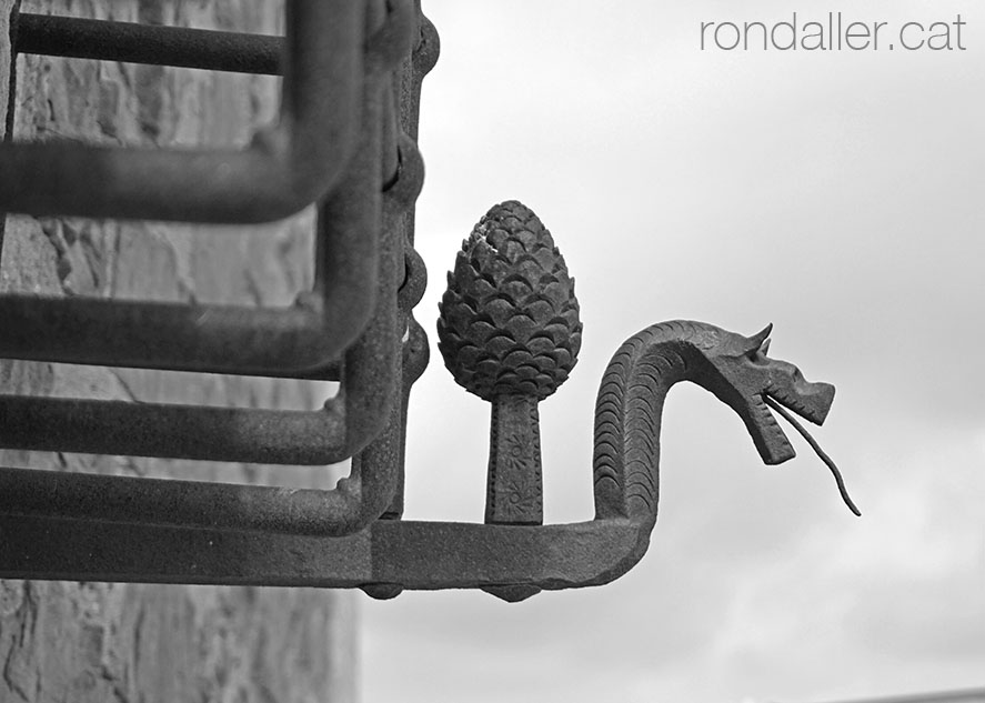 Figura d'un drac i una pinya en una reixa de ferro forjat.