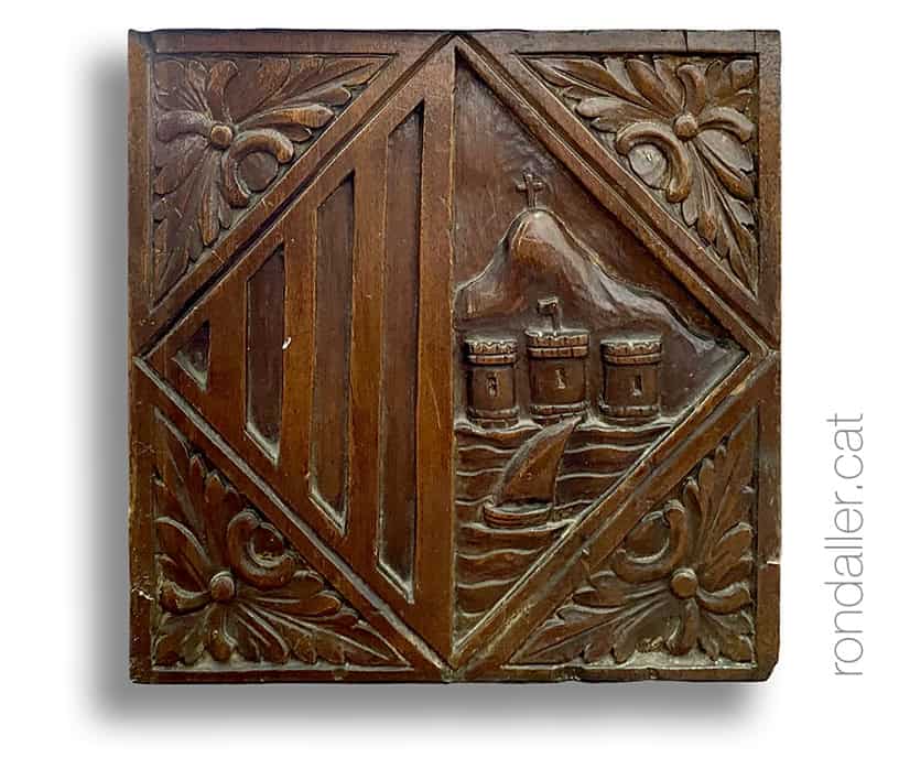 Escut municipal gravat als bans de fusta de la capella del cementiri.