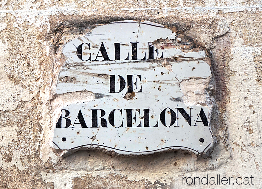 Placa ceràmica molt desgastada amb el nom del carrer de Barcelona.