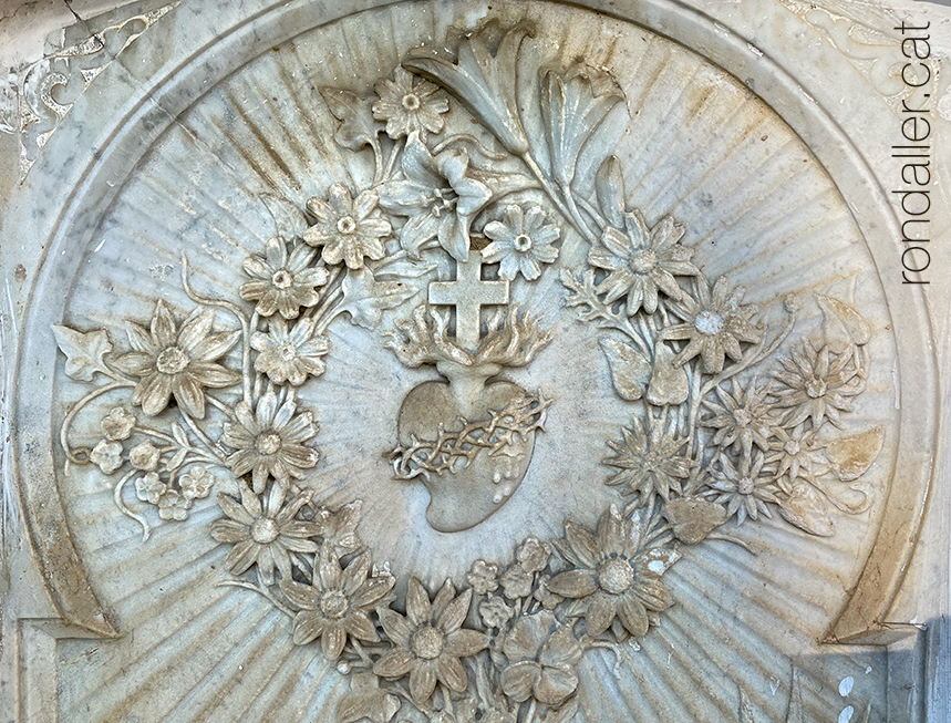 Relleu en una llosa funerària amb la imatge del Sagrat Cor envoltat de flors.