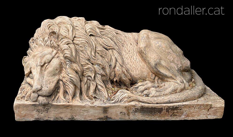 Escultura d'un lleó endormiscat a l'entrada d'un jardí.