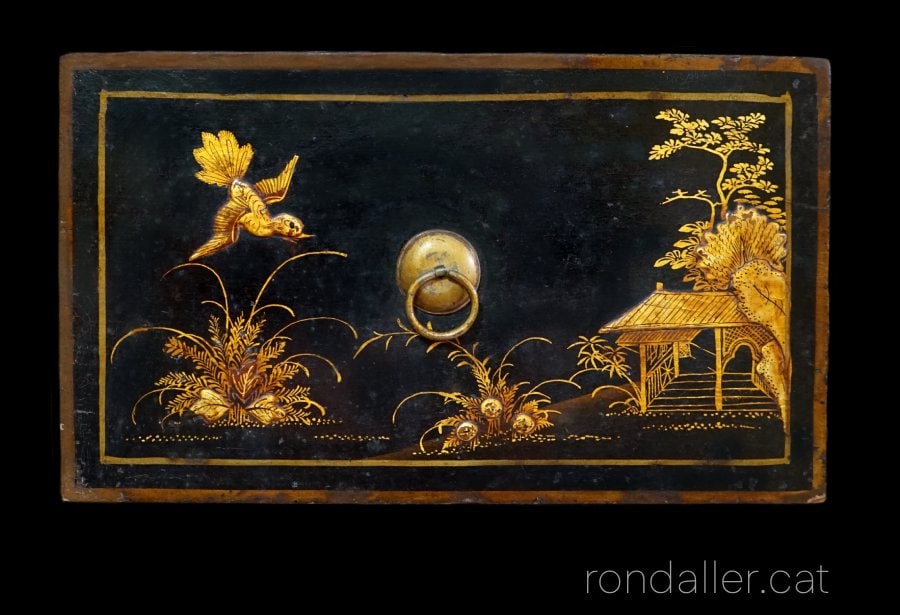 Detall del calaix d'una arquimesa amb motius florals, un ocell i un porxo d'inspiració oriental.