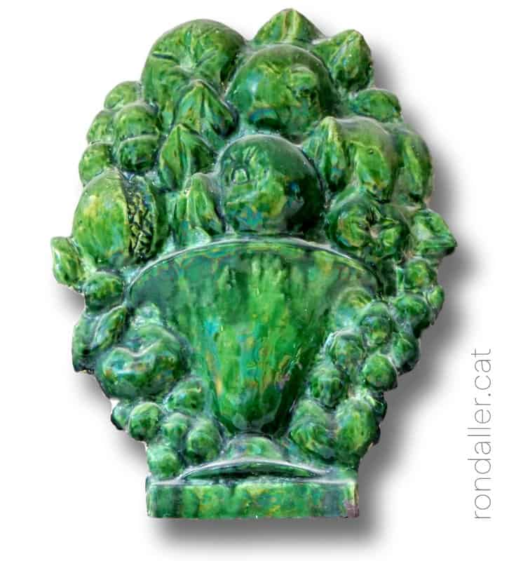 Element decoratiu fet amb ceràmica vidriada de color verd, representant una gerra plena de fruita.